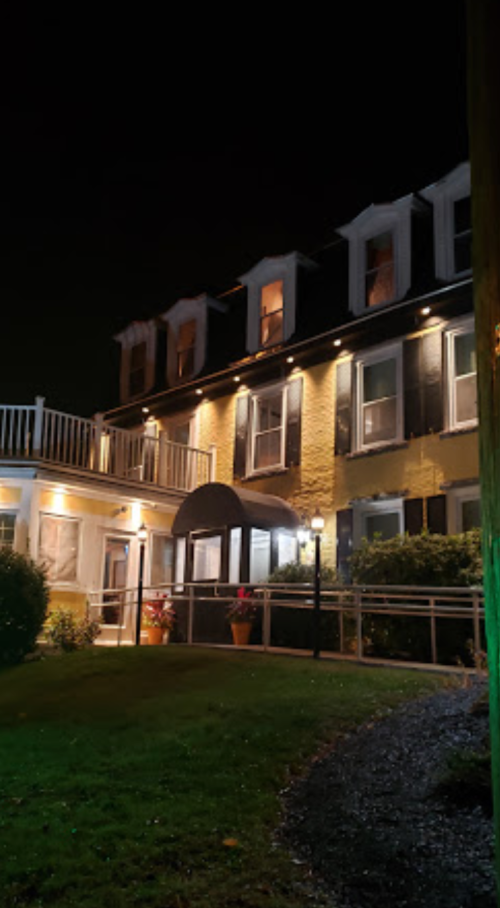 A well-lit, two-story building at night with a porch, multiple windows, and a landscaped yard.