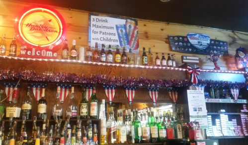 A bar with a variety of liquor bottles, a neon sign, and a banner about drink limits for patrons with children.