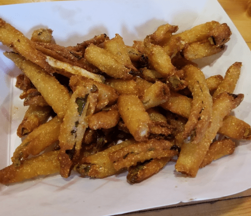 A plate of crispy, golden-brown fried green beans served on a white paper tray.