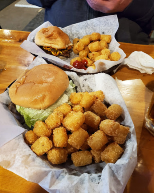 A close-up of a burger with lettuce and a basket of golden tater tots, served on a wooden table.
