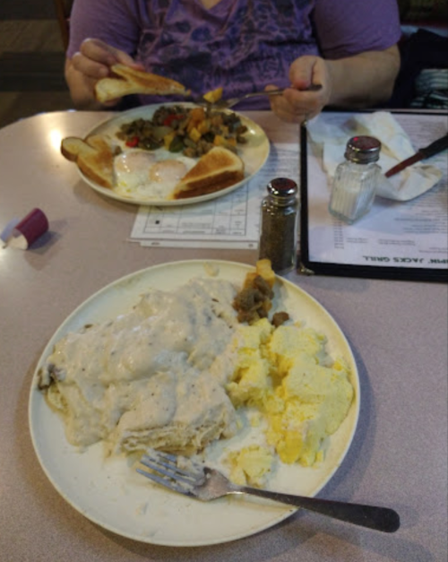 A plate of biscuits and gravy with scrambled eggs and a side of toast, with another plate of mixed vegetables in the background.
