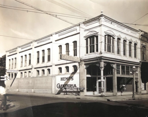 Historic black-and-white photo of a building with "Hemp's Cafeteria" sign, featuring classic architectural details.