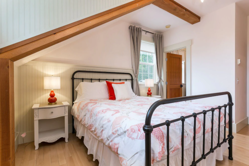 Cozy bedroom with a metal bed frame, light bedding, a nightstand, and a door under a sloped ceiling.
