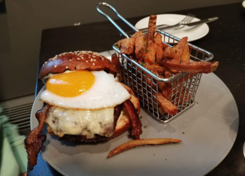 A gourmet burger with a fried egg, cheese, and bacon, served with a side of crispy fries in a small basket.