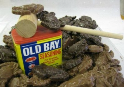 A container of Old Bay seasoning sits atop chocolate crab-shaped candies, with a wooden mallet resting beside it.
