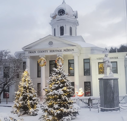 Snow-covered Swain County Heritage Museum with festive trees and decorations, including a Santa figure.