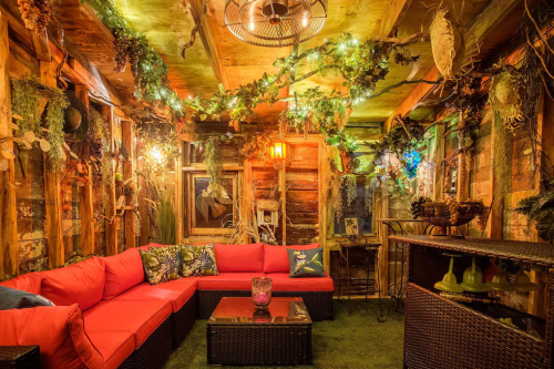 Cozy indoor lounge with red seating, greenery, and warm lighting, creating a rustic, inviting atmosphere.
