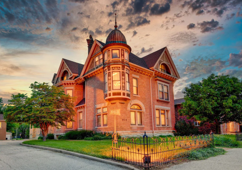A historic brick house with a turret, surrounded by greenery, under a colorful sunset sky.