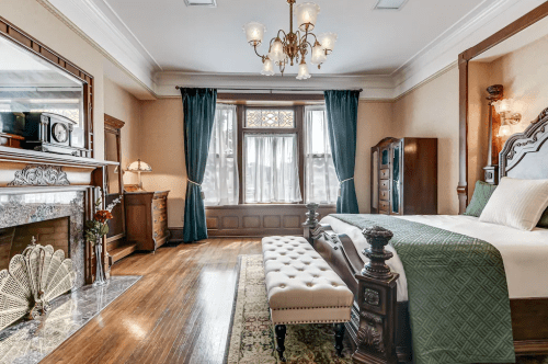Elegant bedroom featuring a chandelier, vintage furniture, and large windows with green curtains. Cozy and inviting atmosphere.