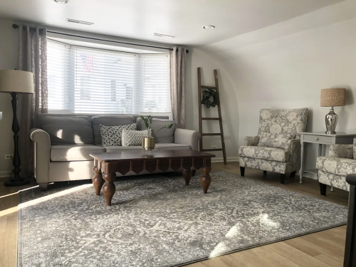 Cozy living room with a gray sofa, patterned chairs, a wooden coffee table, and a large area rug under natural light.
