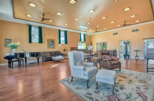 Spacious, well-lit room with a piano, seating areas, and elegant decor, featuring wooden floors and large windows.