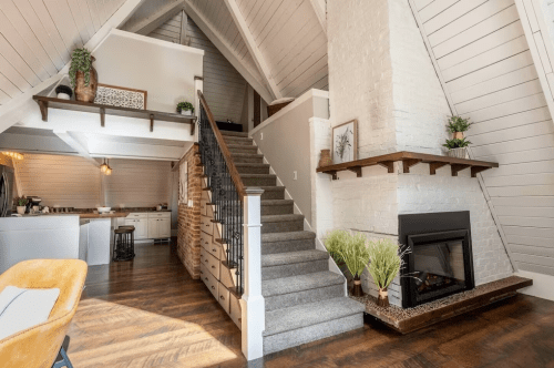 Cozy interior of a modern home featuring a staircase, fireplace, and open kitchen with wooden accents.