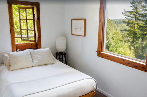 Cozy bedroom with a bed, wooden accents, and large windows showcasing a forest view.