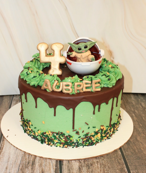 A green birthday cake with chocolate frosting, featuring a Yoda figure, the number 4, and the name "Aubree."