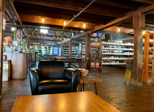 Cozy interior of a rustic store with wooden beams, shelves of products, and a black leather chair in the foreground.
