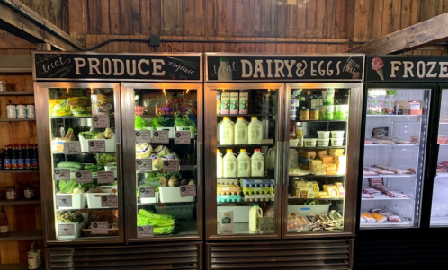 Refrigerated display cases filled with organic produce, dairy, eggs, and frozen foods in a rustic market setting.