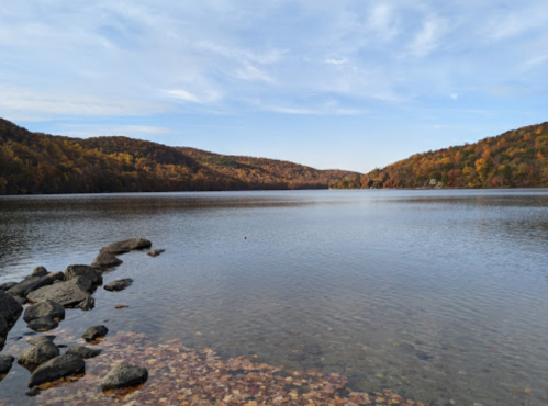 A serene lake surrounded by autumn-colored hills and rocky shores under a clear blue sky.