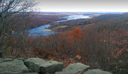 Scenic view of a river winding through autumn-colored trees and hills, with rocky foreground.