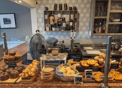 A display of various baked goods, including muffins, cookies, and pastries, in a cozy café setting.