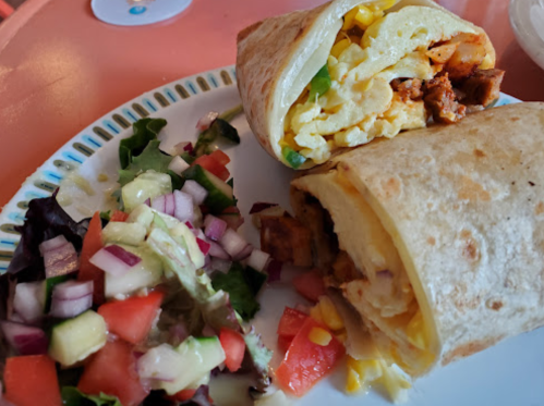 A plate with a cut burrito filled with eggs and chicken, alongside a fresh salad with diced vegetables.