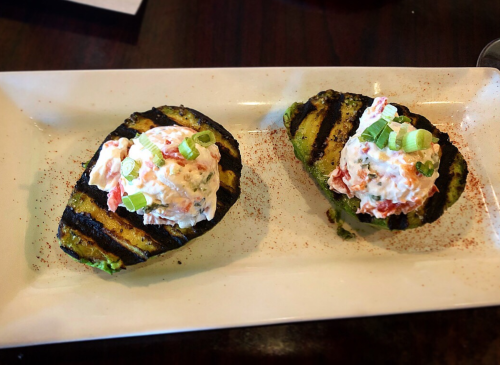 Grilled avocado halves topped with creamy lobster salad and green onions, served on a white plate.