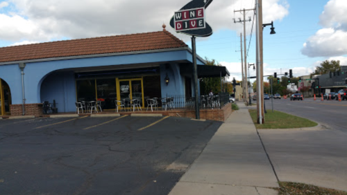 Exterior of a restaurant called "Wine Dive," featuring outdoor seating and a nearby street with traffic.