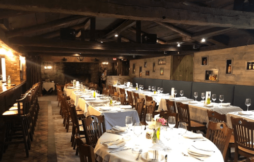 A rustic restaurant interior with wooden beams, tables set for dining, and a cozy atmosphere.