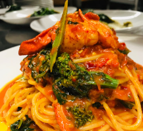 A plate of spaghetti topped with lobster, greens, and a rich tomato sauce, garnished with green onion.