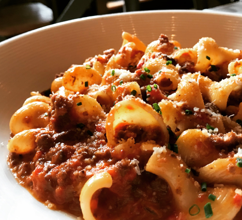 A close-up of a bowl of pasta with meat sauce, topped with herbs and grated cheese.