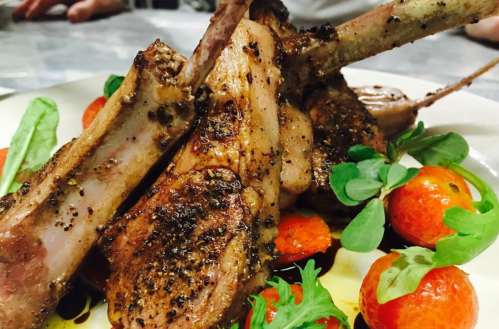 A plate of grilled lamb chops garnished with cherry tomatoes and fresh greens.