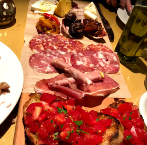 A wooden platter with assorted cured meats, cheeses, and bruschetta topped with diced tomatoes and herbs.