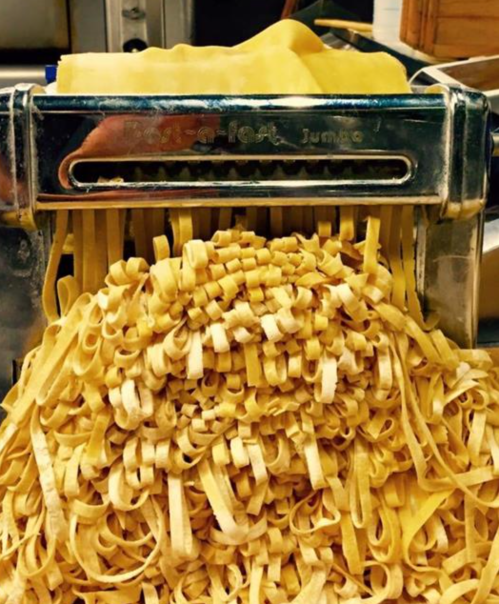 Freshly made fettuccine pasta spilling out of a pasta machine, showcasing its golden color and texture.