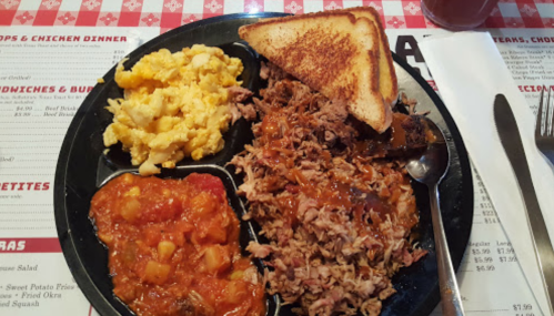 A plate with pulled pork, scrambled eggs, baked beans, and toast on a checkered tablecloth.