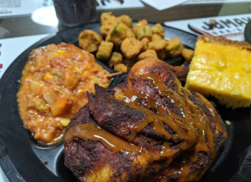 A plate featuring fried chicken with sauce, okra, cornbread, and a side of tomato-based stew.