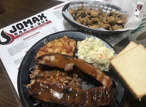 A plate of barbecue ribs, pulled pork, coleslaw, baked beans, and two slices of bread, with a basket of fried pickles.