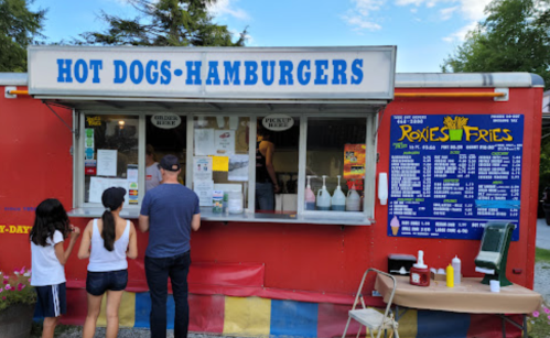A food truck serving hot dogs and hamburgers, with customers ordering at the window and a menu displayed on the side.