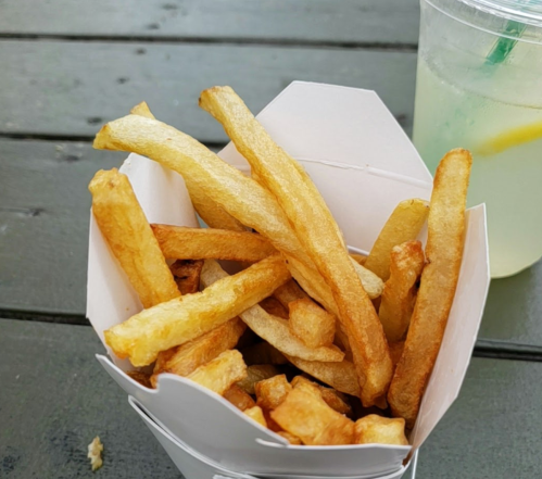 A container of golden, crispy French fries next to a refreshing drink on a wooden table.