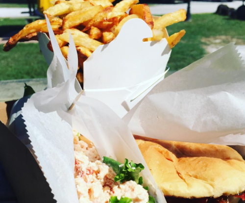 A close-up of a sandwich with lobster salad and lettuce, alongside a container of golden French fries.