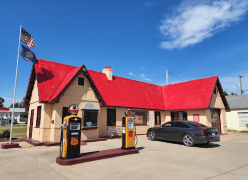 Historic gas station with a red roof, vintage pumps, and flags, set against a clear blue sky.