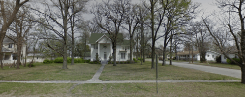 A large white house surrounded by bare trees and a grassy yard, with a quiet street visible in the background.