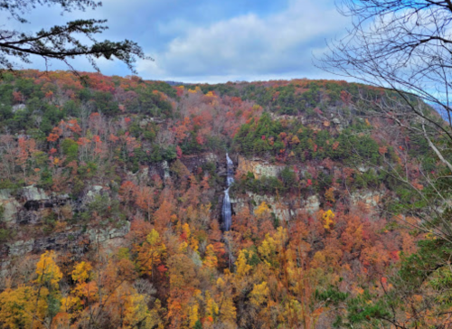 A scenic view of a waterfall surrounded by vibrant autumn foliage in a mountainous landscape.