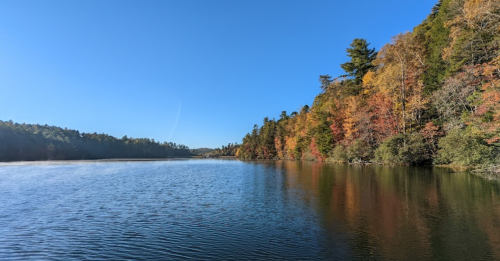 A serene lake surrounded by trees with autumn foliage under a clear blue sky.