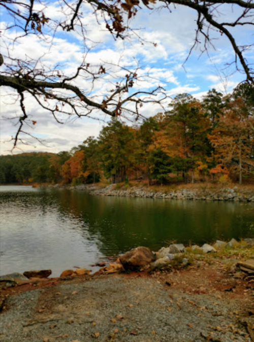 A serene lake surrounded by trees with autumn foliage under a partly cloudy sky.