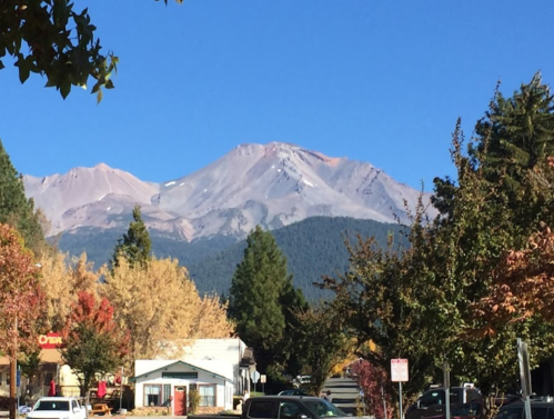 A scenic view of a mountain with a clear blue sky, framed by colorful autumn trees and buildings in the foreground.