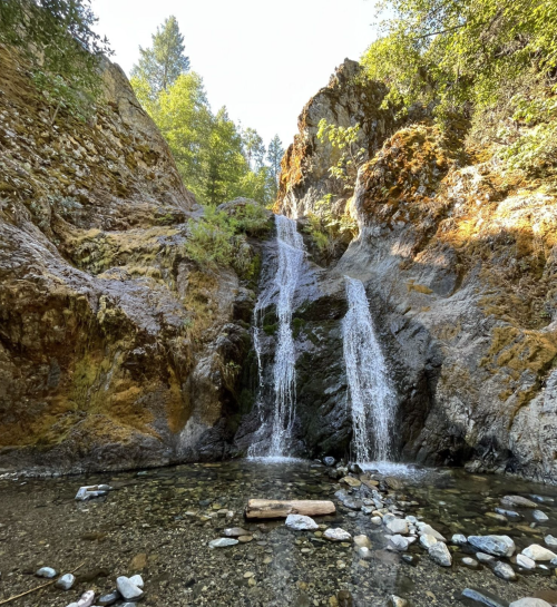 A serene waterfall cascading down rocky cliffs, surrounded by lush greenery and a clear stream below.
