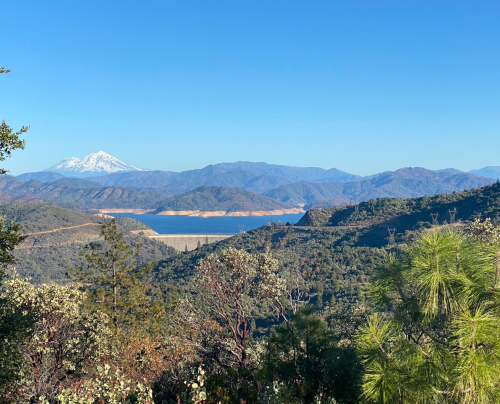 A scenic view of mountains and a lake under a clear blue sky, with a snow-capped peak in the distance.