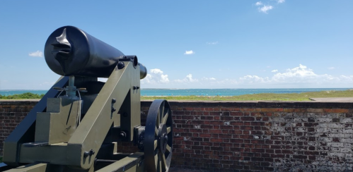 A historic cannon overlooks a scenic coastal view with blue skies and distant land across the water.