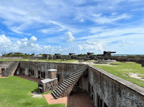 Historic fort with cannons, grassy areas, and stairs under a blue sky with scattered clouds.