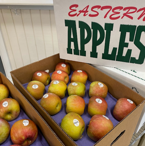Two boxes of Eastern apples with a sign above, showcasing a variety of red and green apples on purple padding.