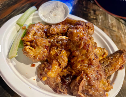 A plate of crispy chicken wings with a side of celery and ranch dressing.